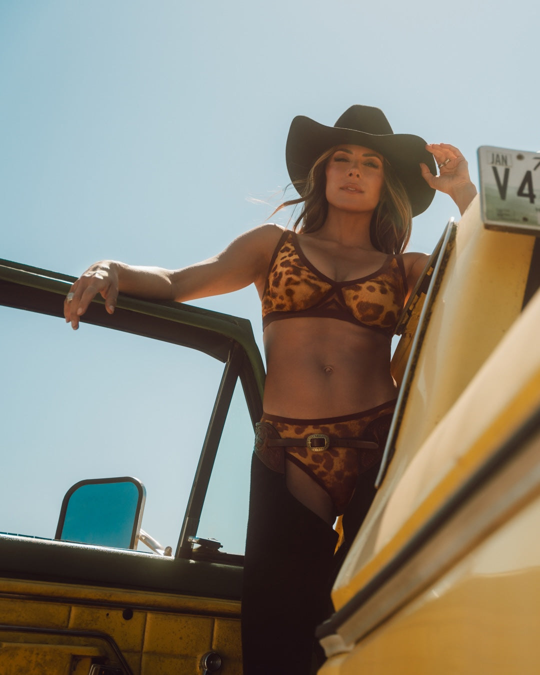 Leopard-print sheer bralette and matching brief set worn with a cowboy hat outdoors.