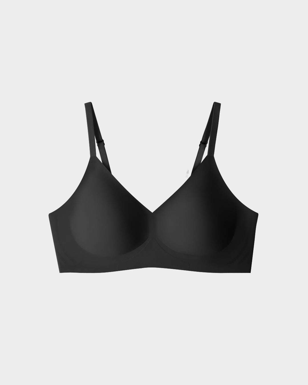 Black seamless wireless bralette with adjustable thin straps and smooth molded cups on grey backdrop.