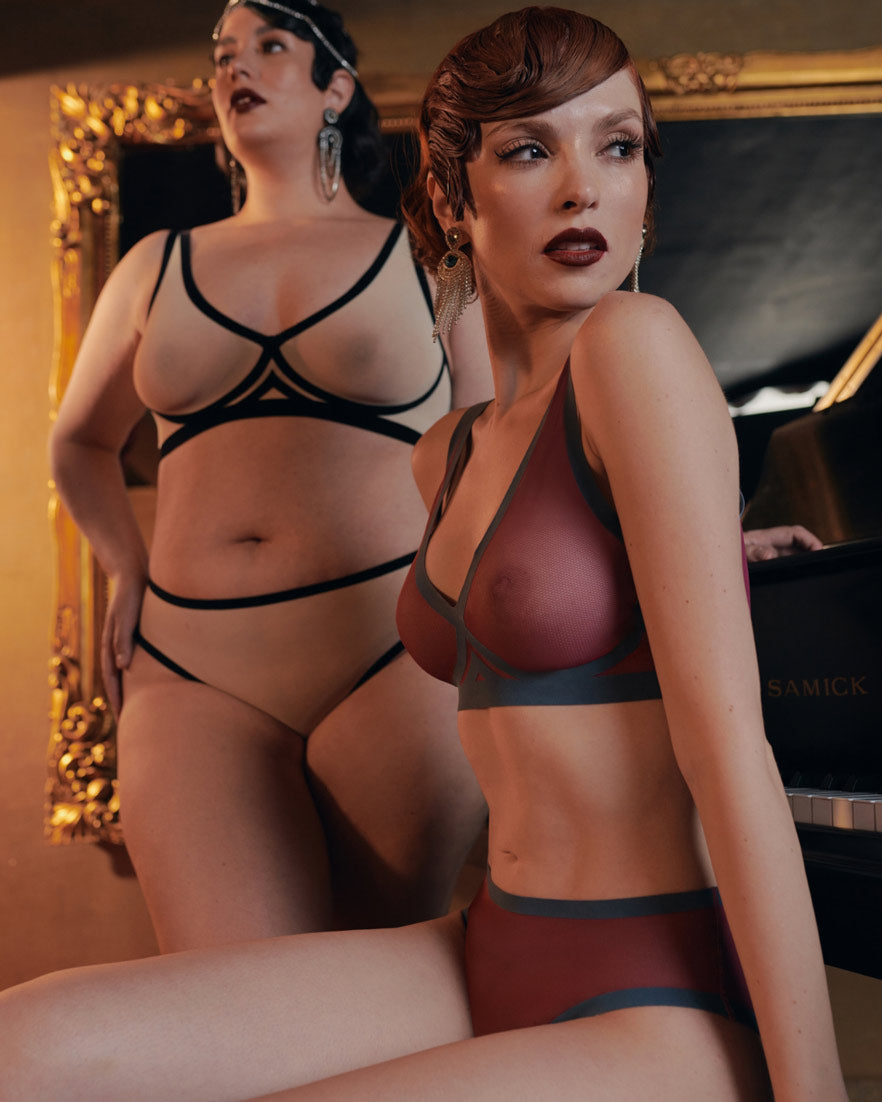 Model wearing cabernet mesh high-waisted panty and matching sheer set beside a grand piano.