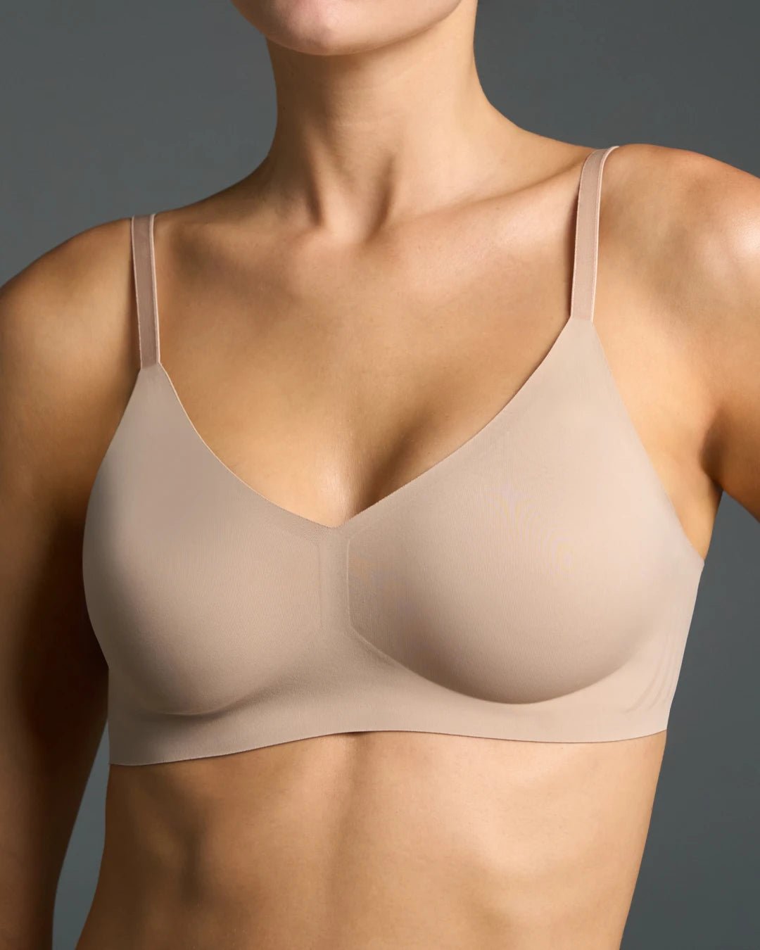 Nude seamless wireless bra with thin adjustable straps and a soft V-neckline, worn on model.